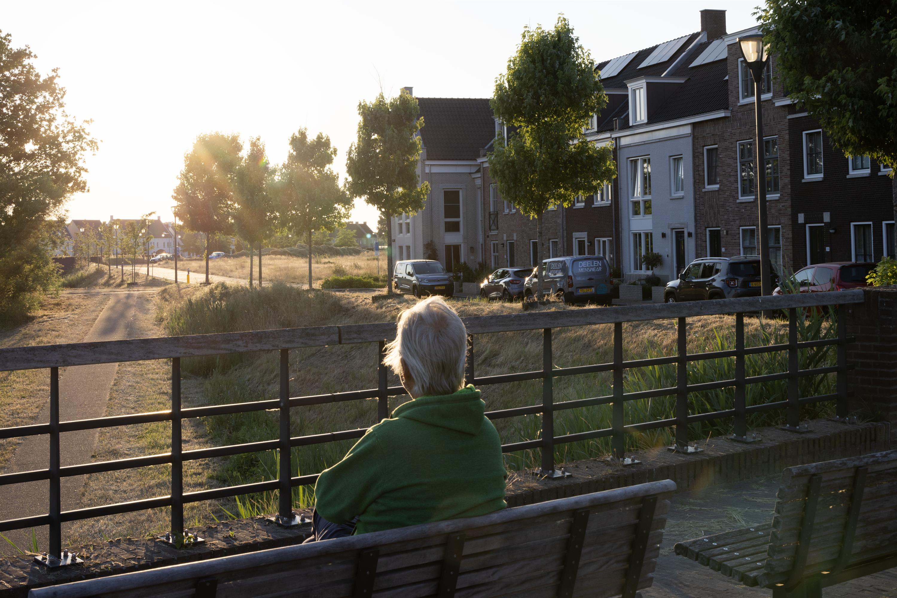 mevrouw, zit op bankje, kijkt naar de omgeving, bomen, woonwijk